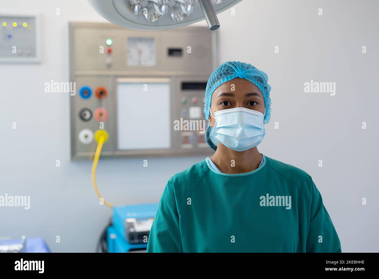 Portrait of biracial female healthcare worker in surgical cap, mask and gown in operating