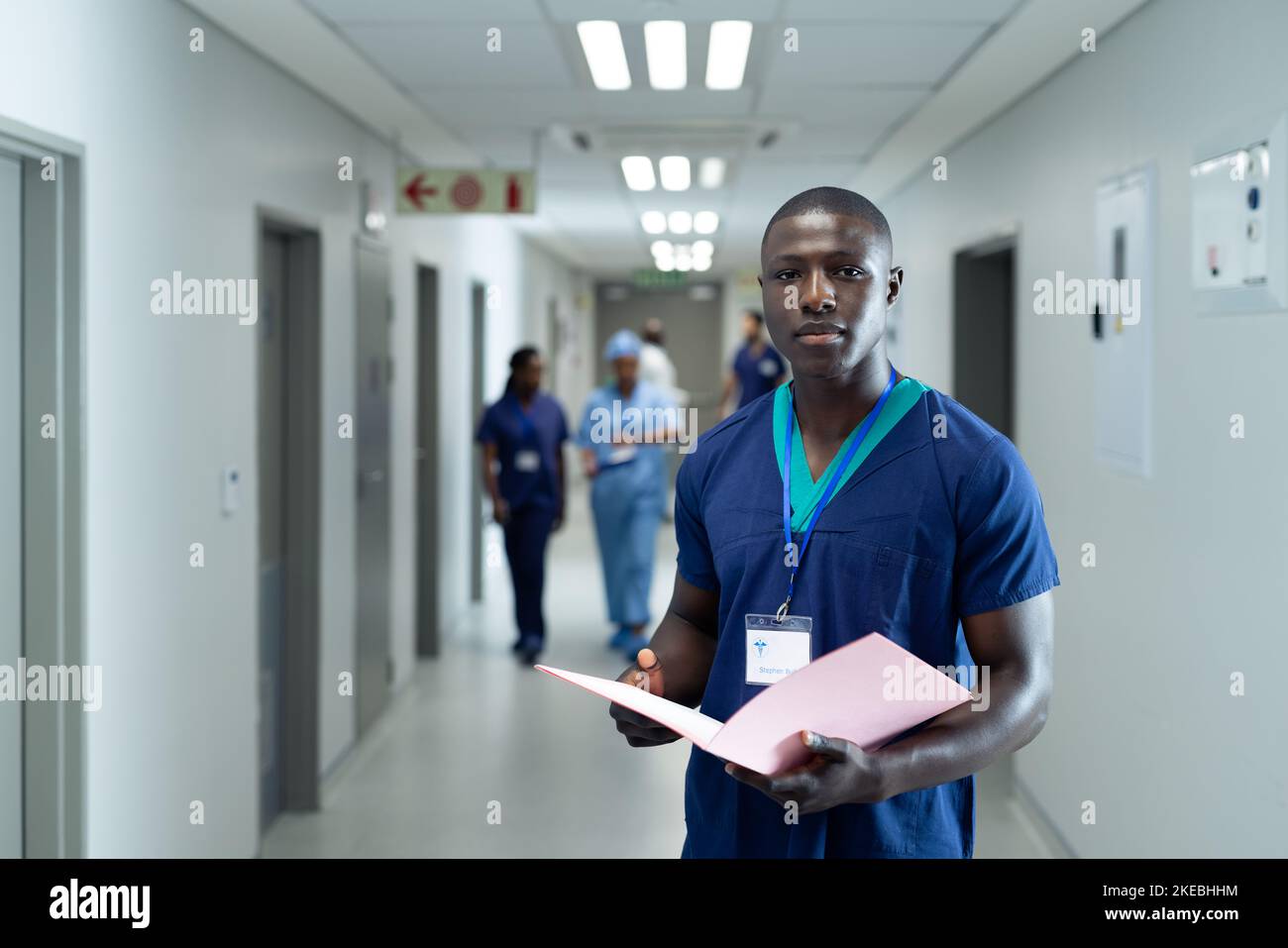 Portrait of african american male healthcare worker with file in busy hospital corridor, copy space. Hospital, medical and healthcare services. Stock Photo