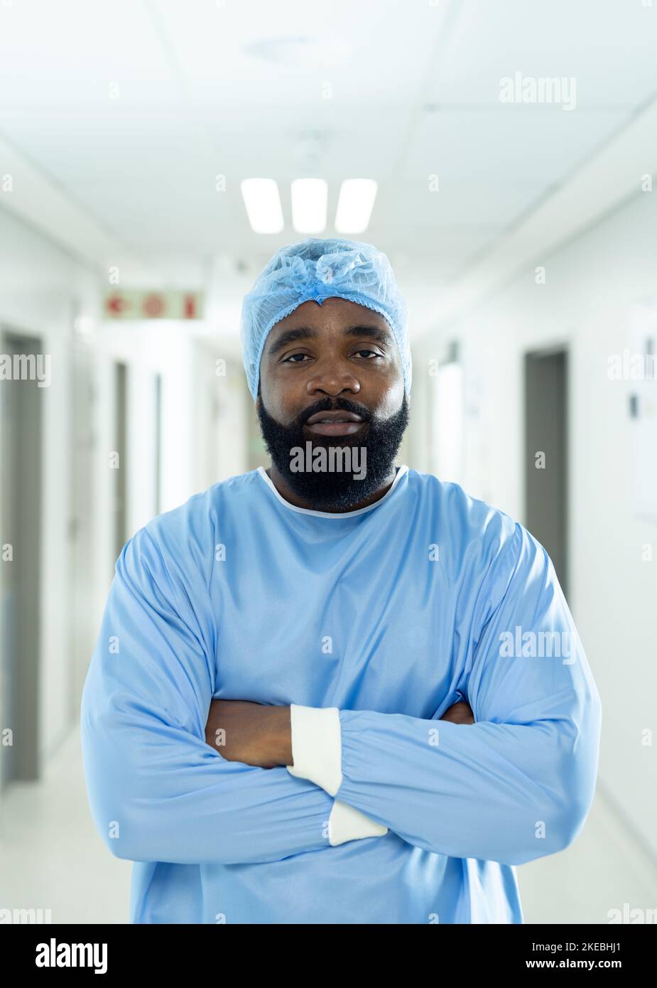 Vertical portrait of biracial male healthcare worker in surgical cap and gown in hospital corridor Stock Photo
