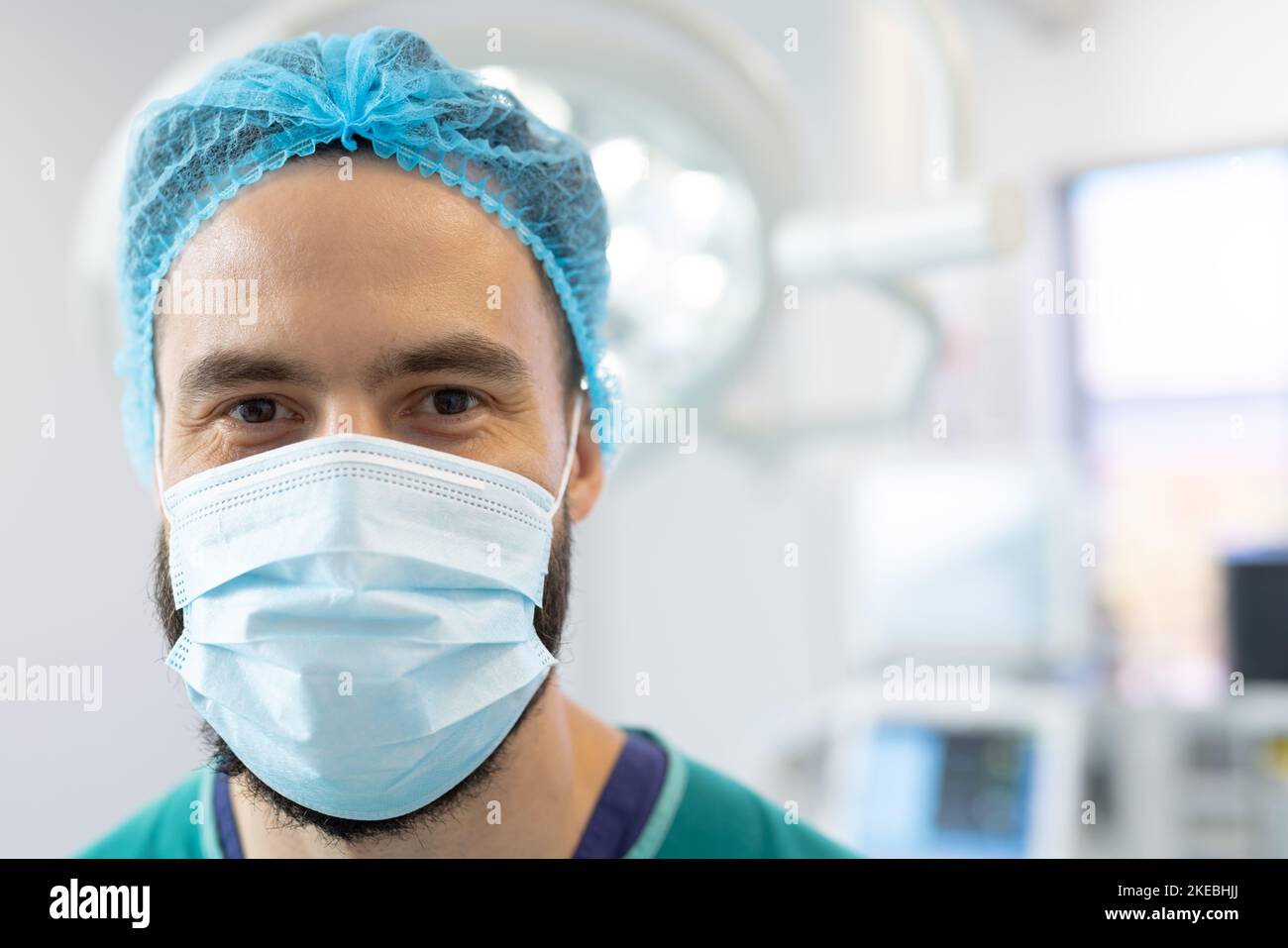 Portrait of smiling caucasian male surgeon in surgical mask and cap in operating theatre, copy space. Hospital, medical and healthcare services. Stock Photo