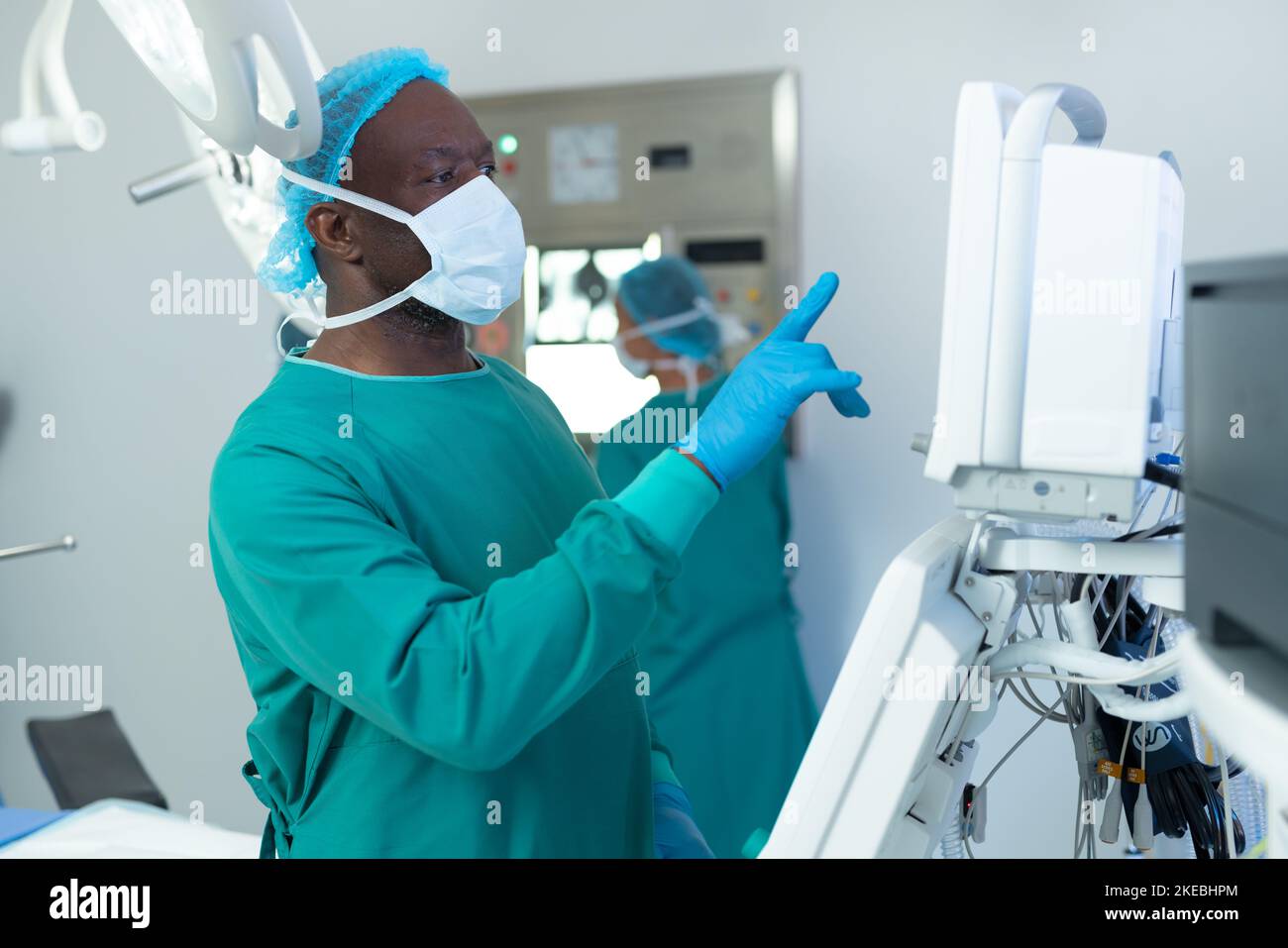 African american male surgeon operating computerised medical equipment in operating theatre. Hospital, medical and healthcare services. Stock Photo