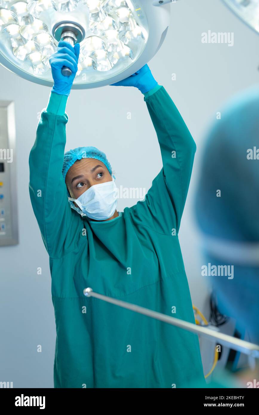 Vertical of biracial female surgeon adjusting lights in operating theatre for operation, copy space. Hospital, medical and healthcare services. Stock Photo