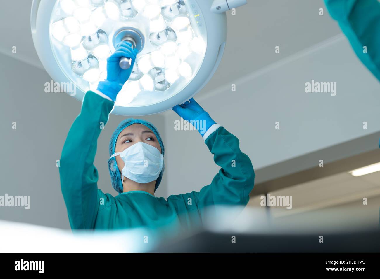 Asian female surgeon adjusting lights in operating theatre for operation, with copy space. Hospital, medical and healthcare services. Stock Photo