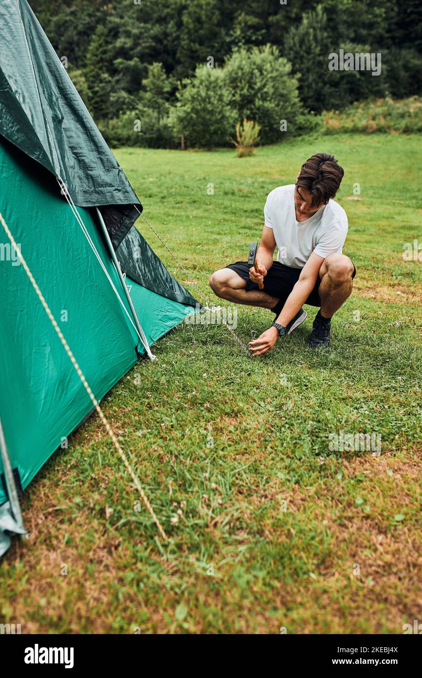 Young man putting up a tent on camping during summer vacation trip
