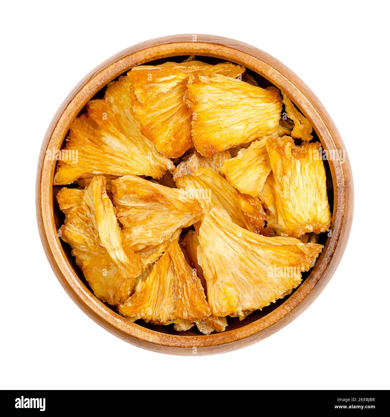 Dehydrated pineapple pieces, in a wooden bowl. Chunks of dried fruits of Ananas comosus, used as snack, for muesli or trail mixes. Stock Photo