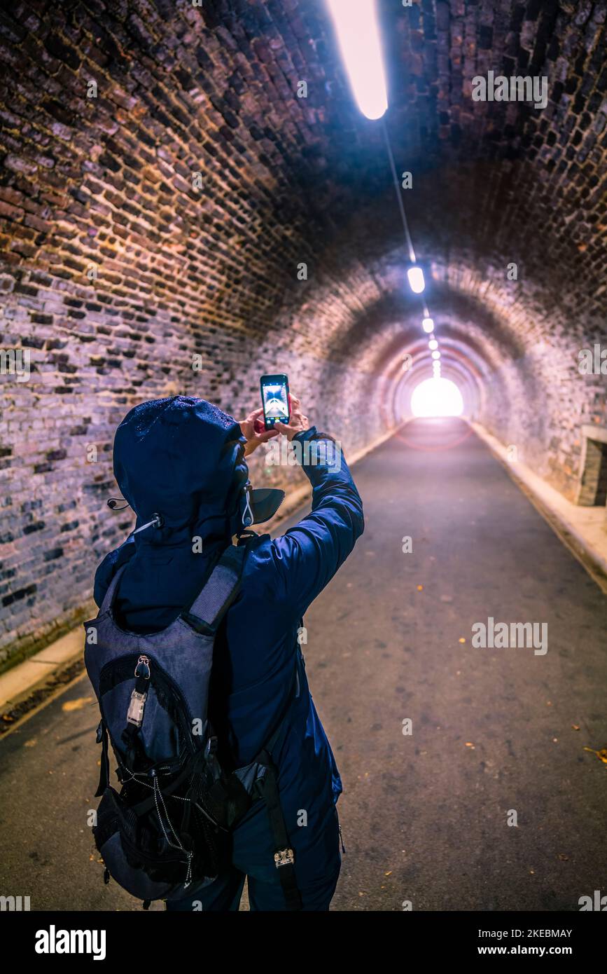 Female photographing in a tunnel on the Keswick rail trail with her mobile phone, English Lake District. Stock Photo