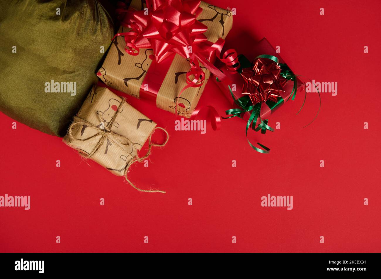 In the corner of a red background there are Christmas gift boxes and satin green bag. New Year's event. Xmas. Boxing Day Stock Photo