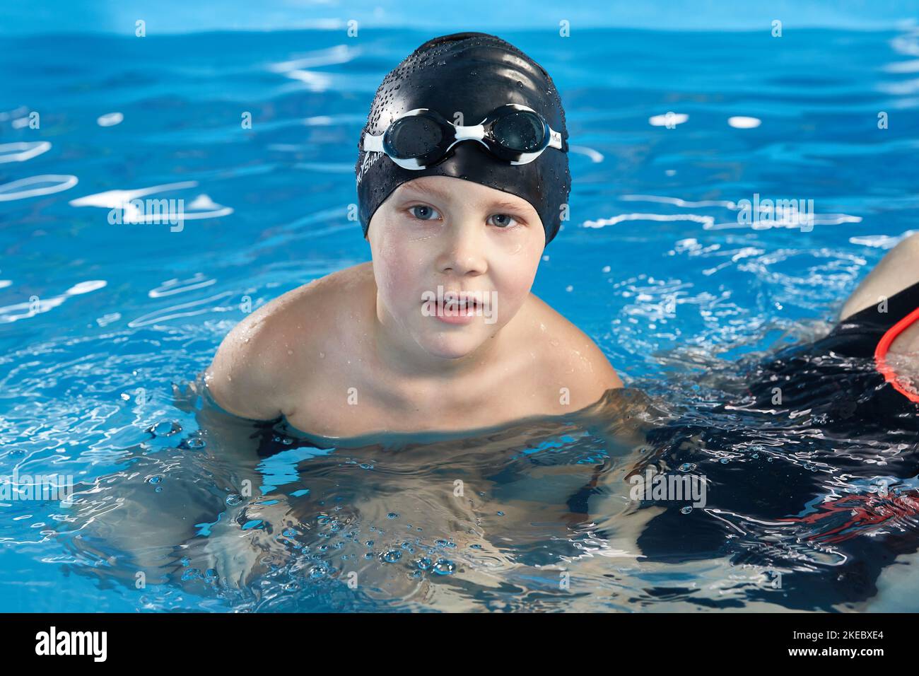 Preschool boy learning how to swim in a pool wearing swimming cap and