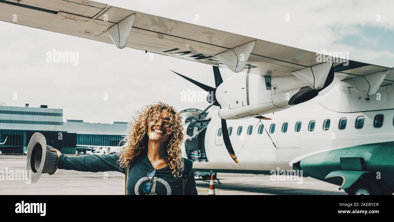 Woman smile and celebrate the arrival at her summer holiday travel vacation destination. Happy female people portrait with airplane flight in background inside the airport. Wanderlust lifestyle Stock Photo