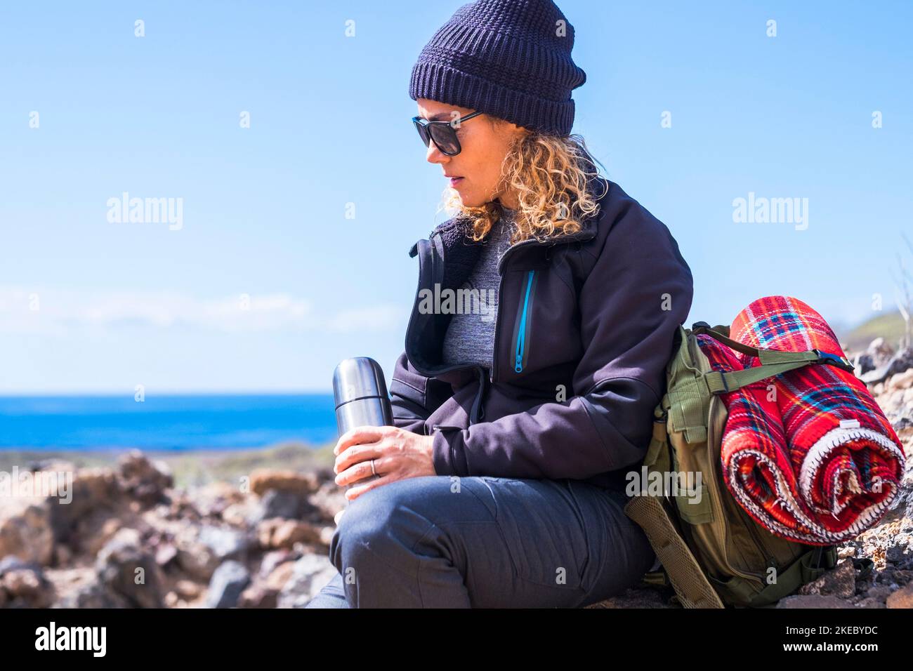 Cute sporty woman enjoy travel and adventure leisure outdoor activity alone sitting on the rocks and drinking to restore energy. Alternative lifestyle with nature and exploring outdoors. Backpack Stock Photo