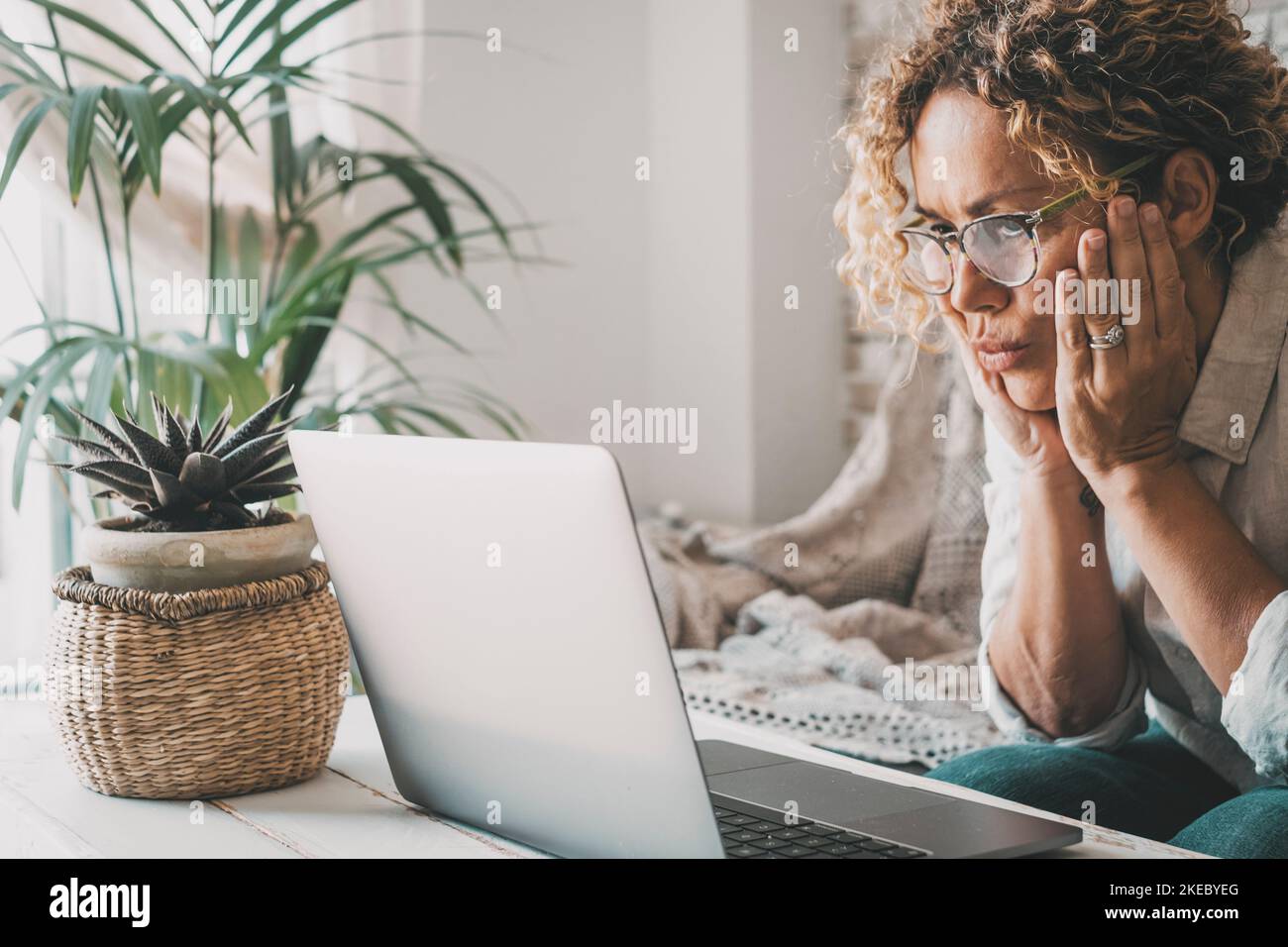 People and problems with computer concept. Woman looking laptop display with worried expression on face. Adult female read bad notification on notebook at home. House leisure activity online. Eyewear Stock Photo