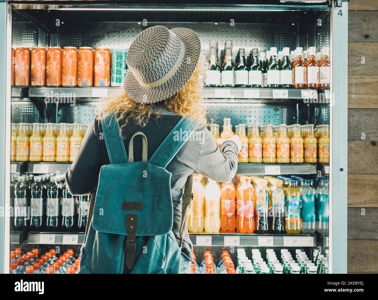 Back view of woman tourist with backpack in front of a window store full of drinks bottles choosing one to buy and drink. Concept of travel solo female people in front of an automatic machine Stock Photo