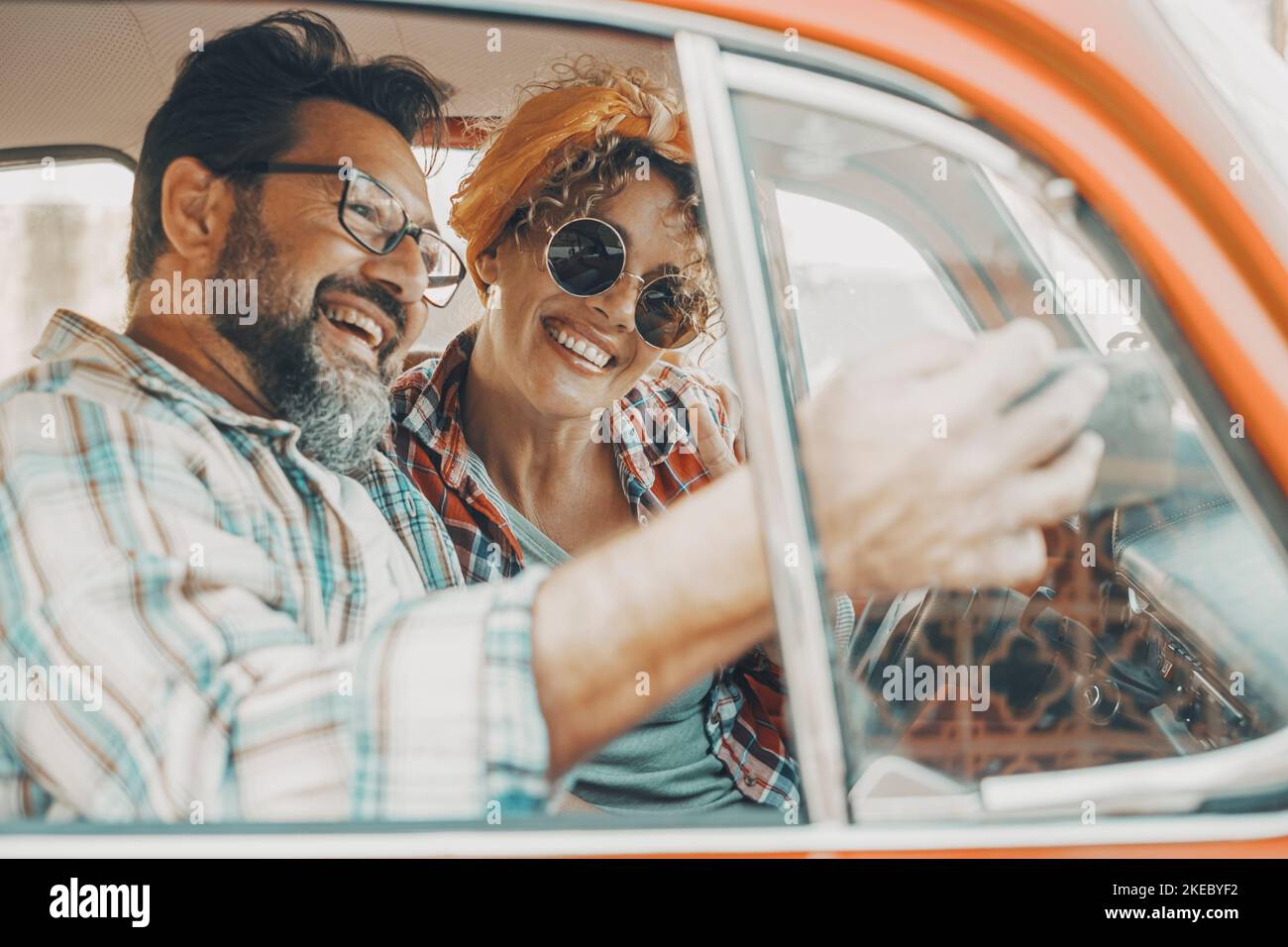 Happy couple having fun inside a car during travel adventure. Cheerful man and woman smiling and laughing a lot together. People enjoying vehicle trip in friendship and relationship. Concept of drive Stock Photo