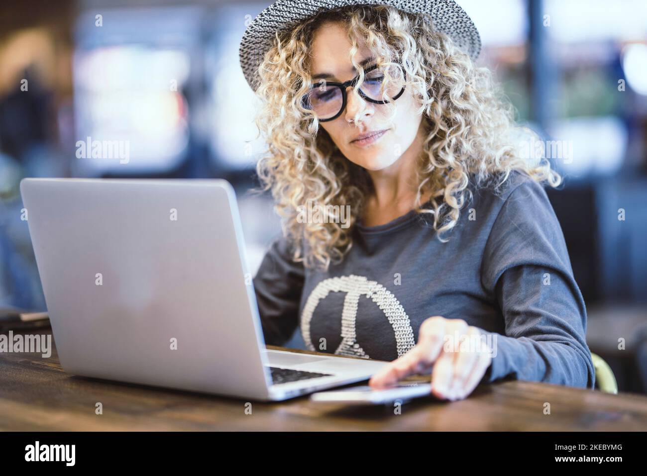 Portrait of woman working with computer in a cafe or airport gate station. Digital nomad and modern worker. Female people using notebook and phone in alternative office. Pretty lady with eyewear Stock Photo