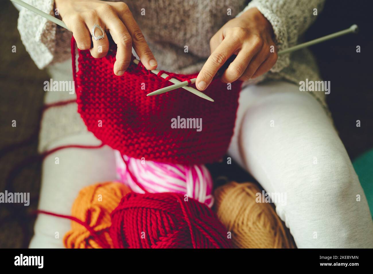 Close up view of fmale hands doing knit work with red wool. Handmade and hand craft clothes production in indoor hobby leisure activity. Woman working with knitting needles. Diy winter activity indoor Stock Photo
