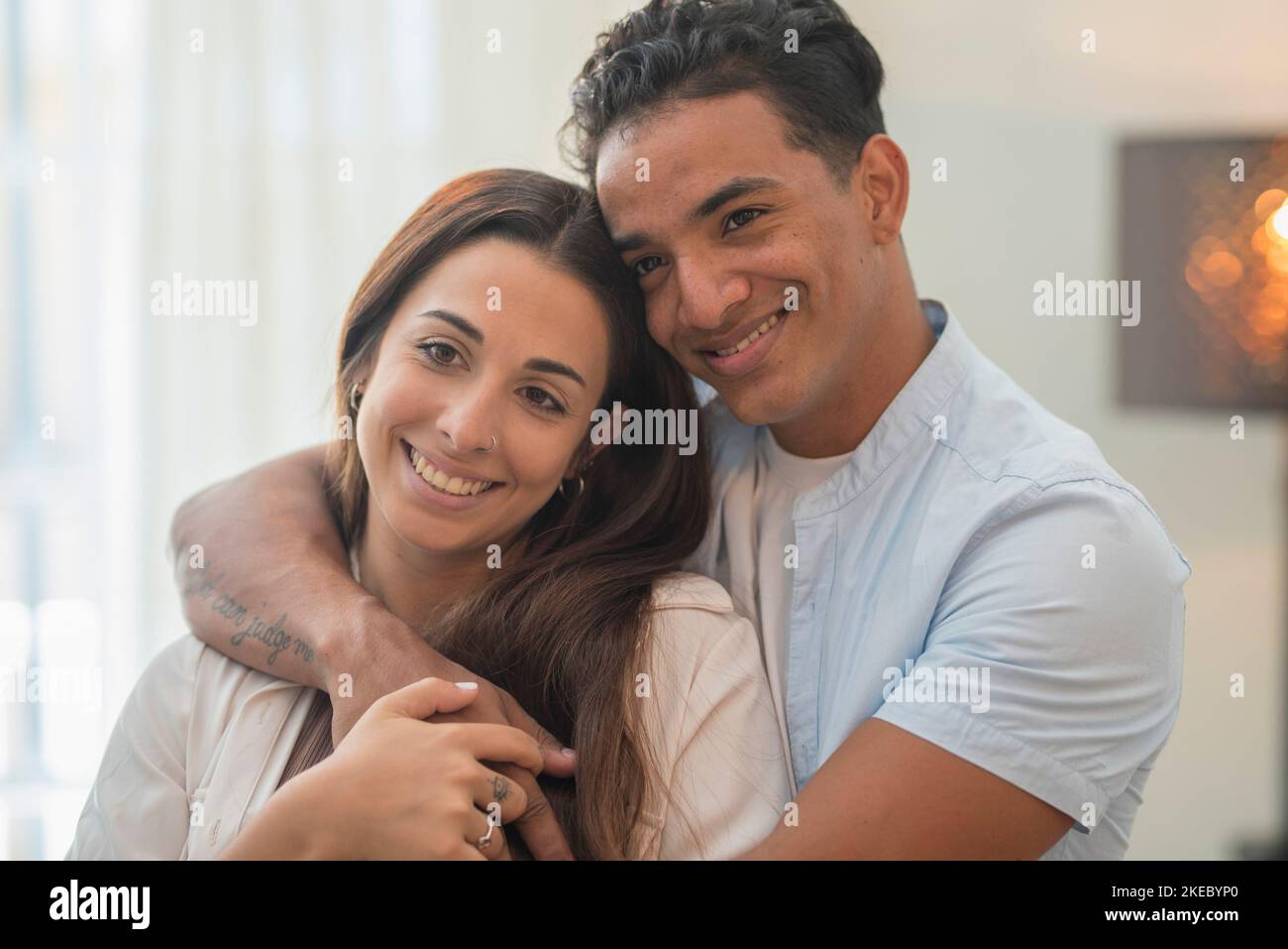 Concept of young interracial couple in love and relationship. Boy hug and protect girlfriend at home. Life and future together man and woman. New apartment happiness satisfaction portrait. Smile Stock Photo
