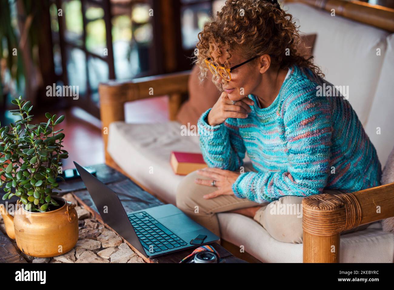 Side view of young woman using laptop sitting on the couch in indoor home leisure modern activity. Online job and surfing the web. Female people use computer and have relax during work. Modern life Stock Photo