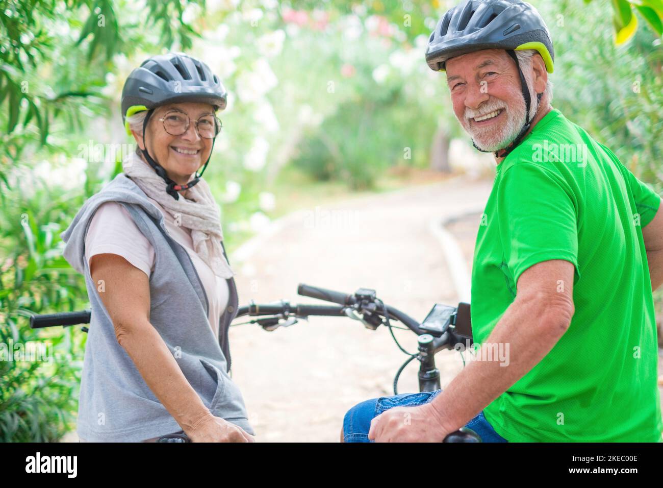 Two happy old mature people enjoying and riding bikes together to be fit and healthy outdoors. Active seniors having fun training in nature. Portrait of two senior looking at the back looking at the camera Stock Photo