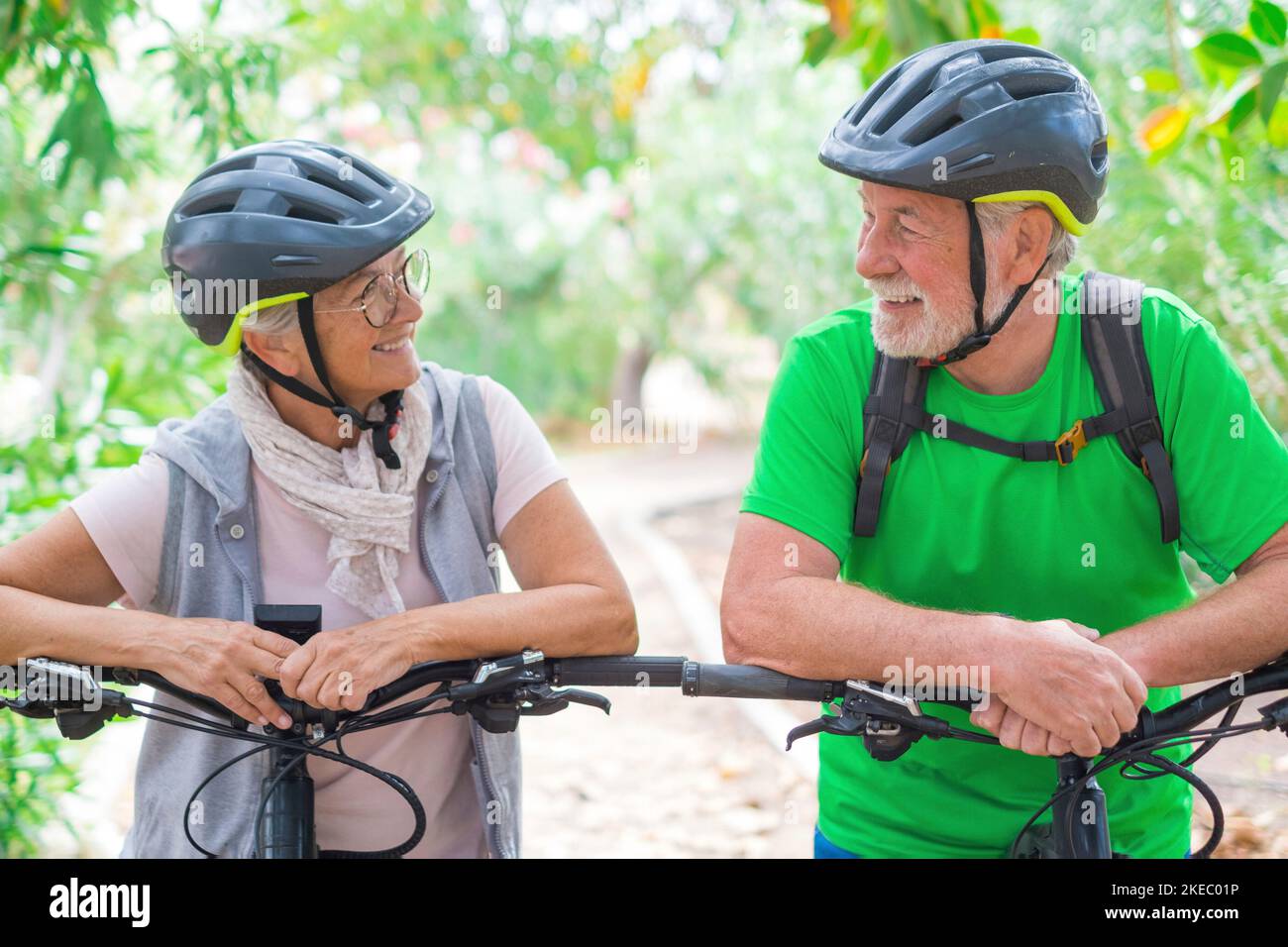 Portrait of couple of old and happy in love seniors looking each other smiling and having fun with their bikes in the nature outdoors together feeling good and healthy. Stock Photo