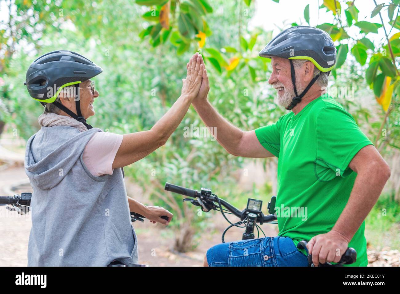 Couple of two seniors giving five together outdoors having fun with bicycles enjoying nature. Couple of old people building a healthy and fit lifestyle. Stock Photo