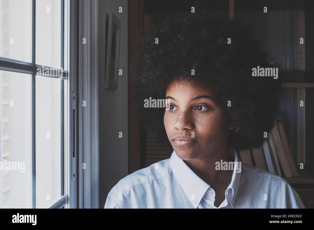Serious african american businesswoman in thoughts looking out through office window. Female executive in deep thought with curly hair thinking for a solution to her problem. Thoughtful lady at workplace Stock Photo