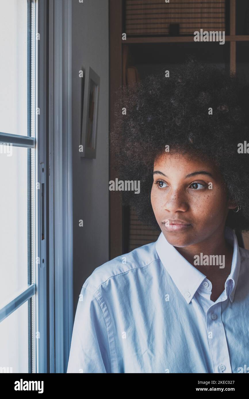 Serious african american businesswoman in thoughts looking out through office window. Female executive in deep thought with curly hair thinking for a solution to her problem. Thoughtful lady at workplace Stock Photo