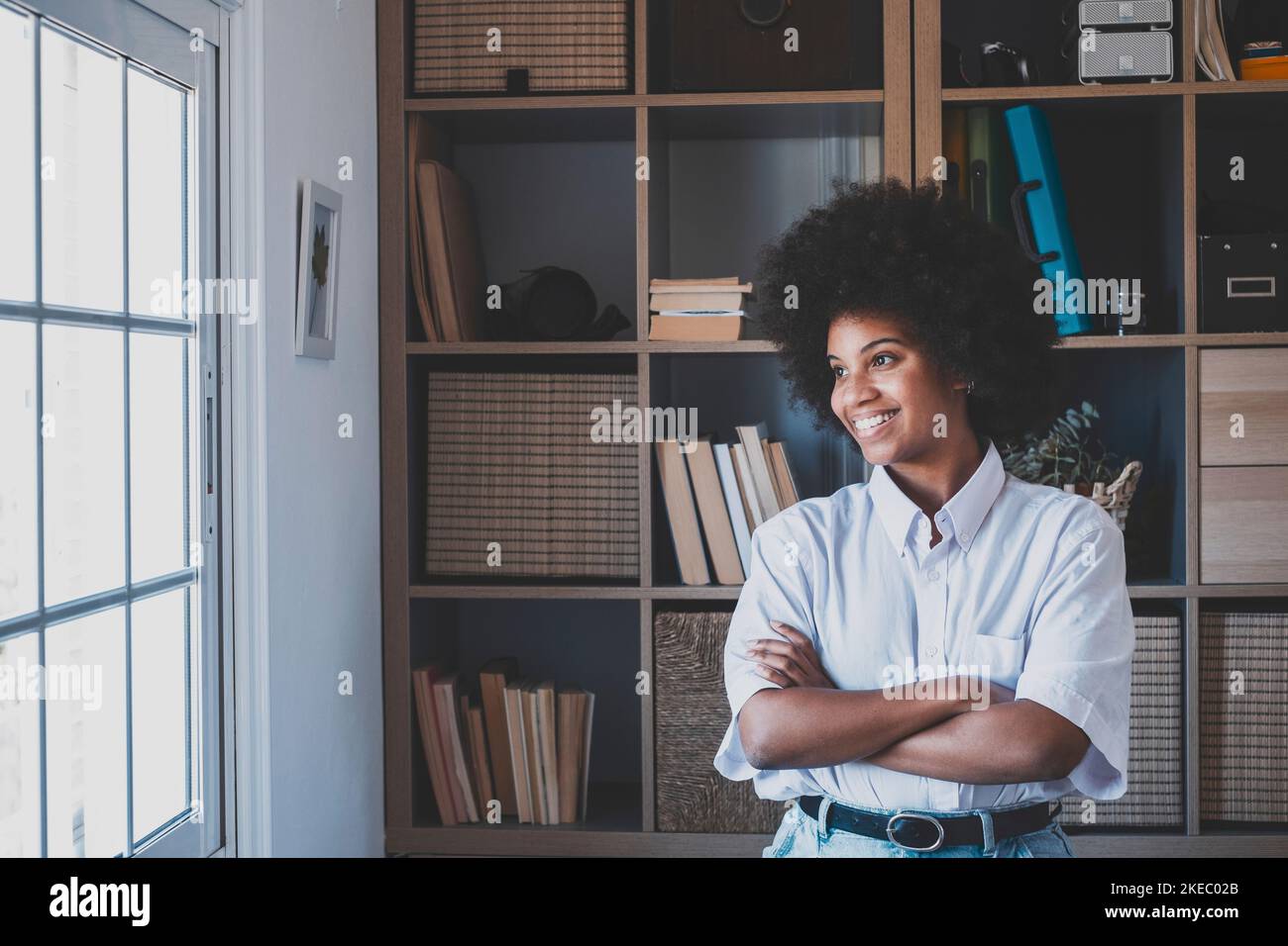 Attractive dark skinned young woman with curly Afro hairstyle looking out through window. Thoughtful african american businesswoman looking away at office. Female lady dreaming about future Stock Photo