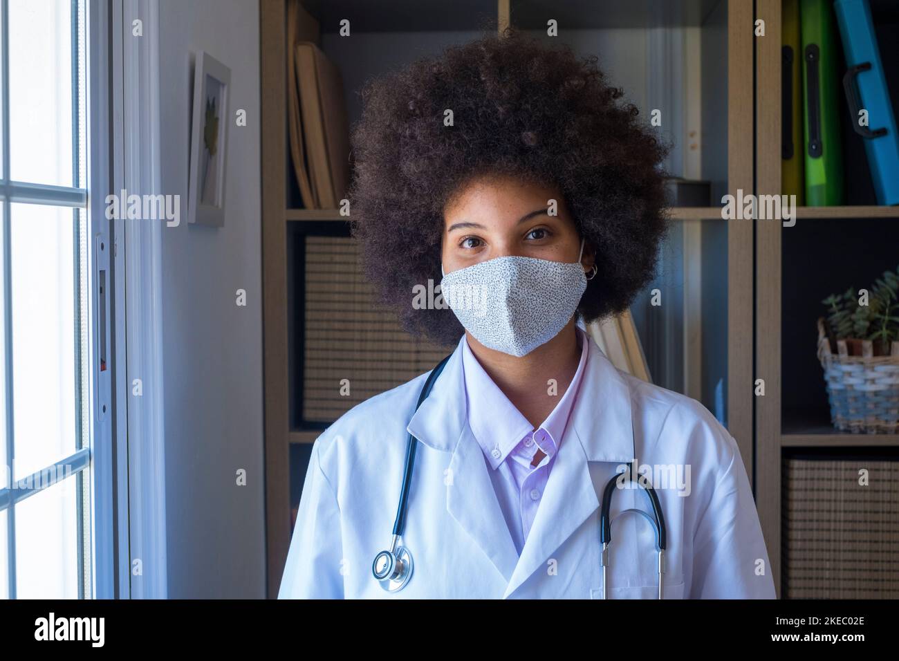 Woman healthcare worker in medical facial cover to protect self from coronavirus outbreak. Portrait of professional african american female doctor wearing protective medical face mask and uniform looking at camera Stock Photo