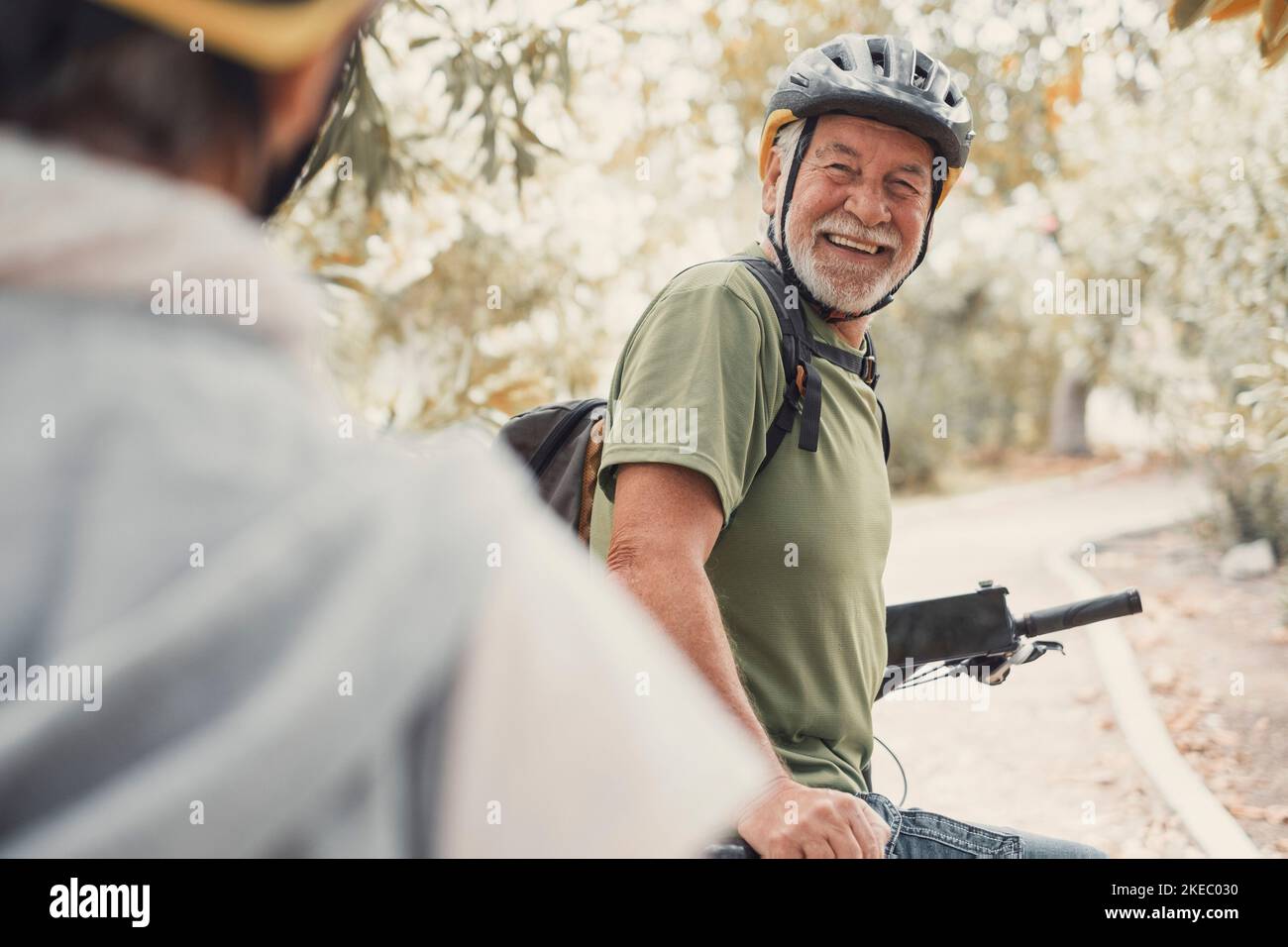 Two happy old mature people enjoying and riding bikes together to be fit and healthy outdoors. Active seniors having fun training in nature. Portrait of one old man smiling in a bike trip with his wife. Woman indicating something and looking at it. Stock Photo