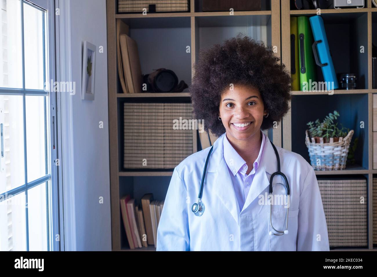 Happy female african american doctor with stethoscope at her clinic. Confident frontline heathcare worker smiling while looking at camera. Young doctor wearing lab coat with stethoscope at hospital office Stock Photo