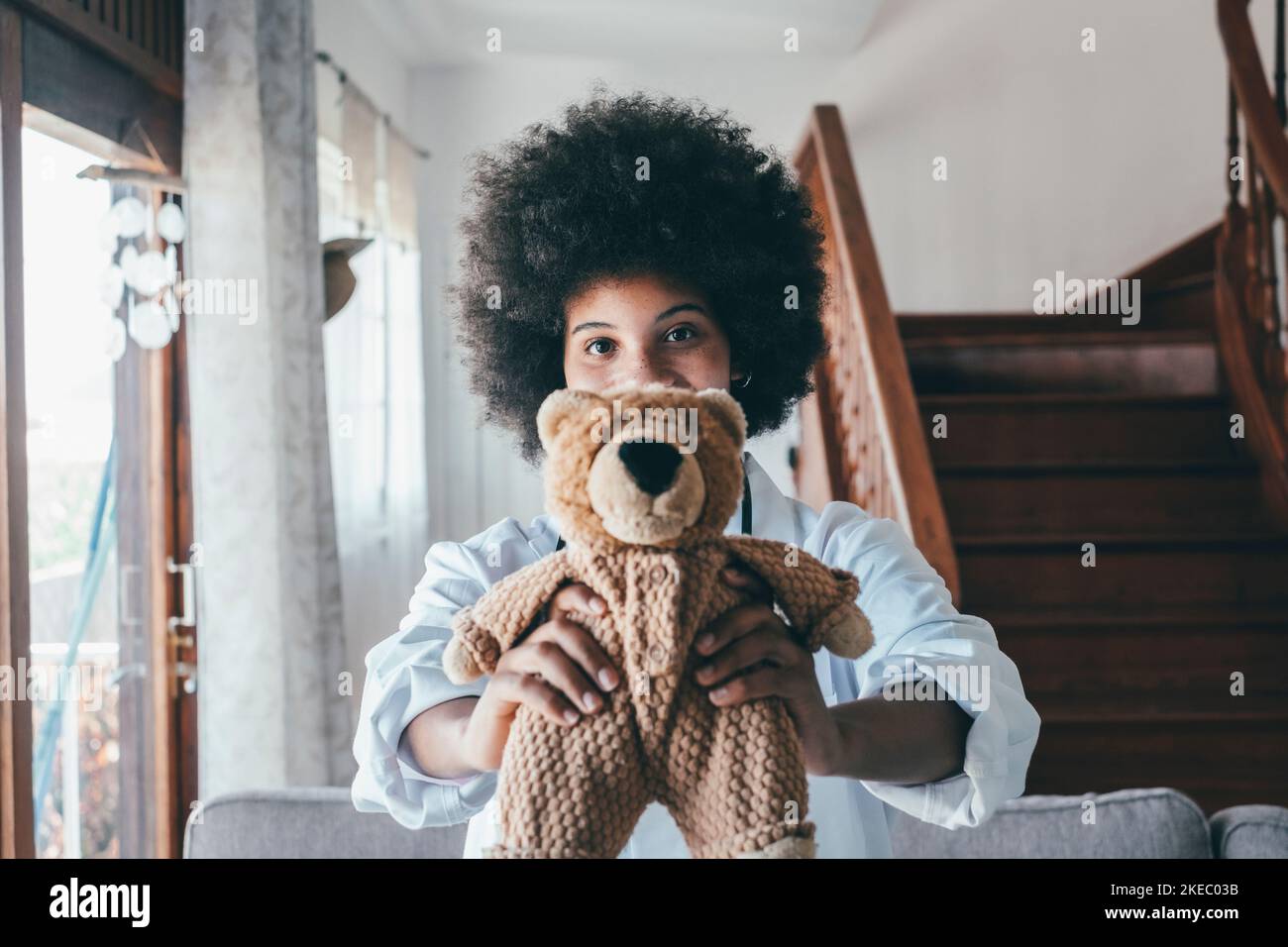 Portrait of young african american female nurse in medical uniform holding stuffed toy showing care love to little patient, happy woman doctor pediatrician posing with teddy bear in hospital or clinic Stock Photo