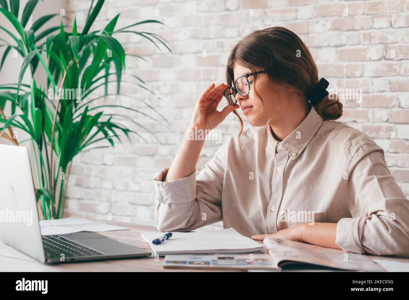 Tired bored teenage girl school student feeling headache or fatigue doing homework at home. Exhausted depressed sick teenagertaking off glasses worried about difficult education problems concept. Stock Photo