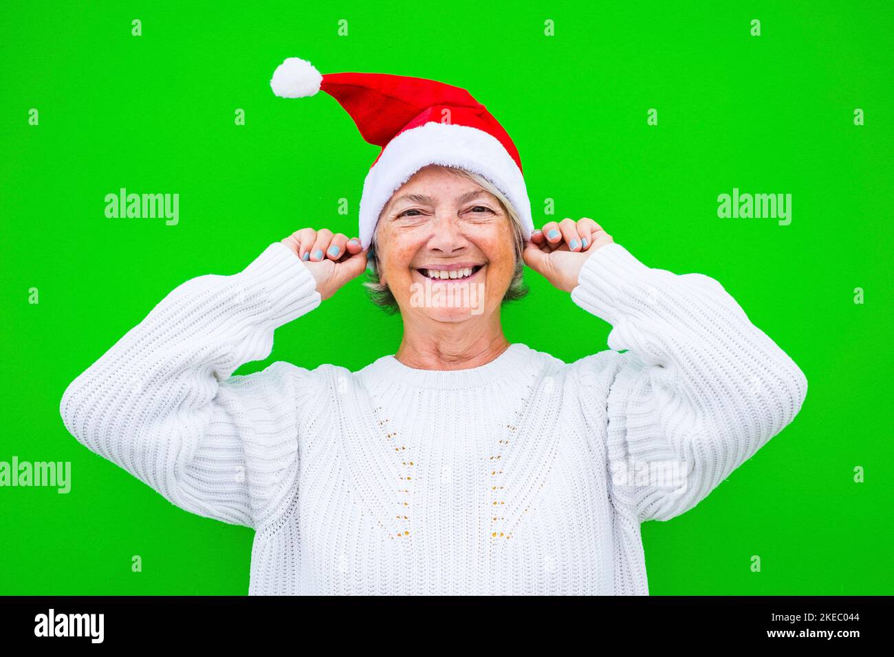portrait and close up of old and mature woman smiling and having fun looking at the camera wearing christmas clothes with green background Stock Photo