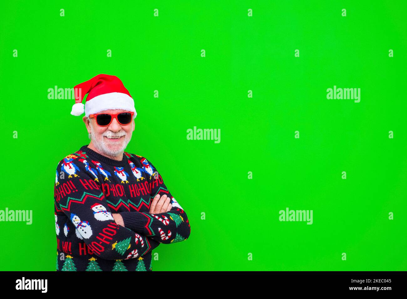 close up and portrait of mature and old man or senior smiling and looking at the camera wearing christmas clothes and hat with green background with copy space Stock Photo