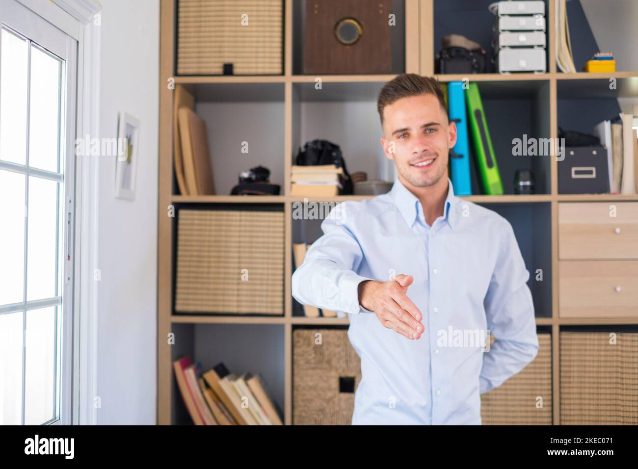 Portrait of smiling handsome businessman extending hand for handshake at camera. Friendly caucasian man greeting or welcoming by offering a to shake hands with client at corporate meeting Stock Photo