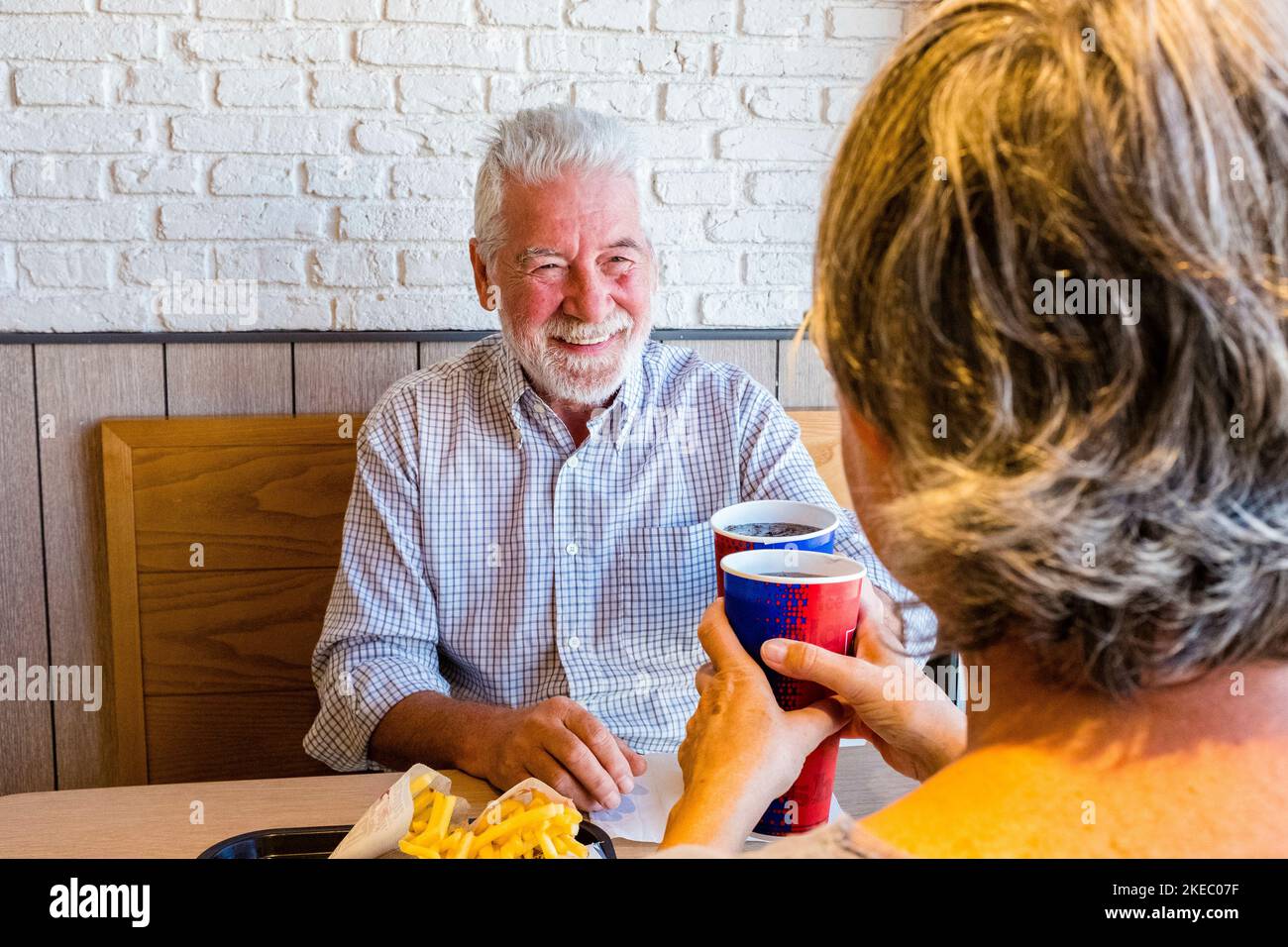 couple of pensioners eating together at fast food or restaurant - seniors meeting in their first date clinking withg the cup - man smiling looking at the mature woman Stock Photo
