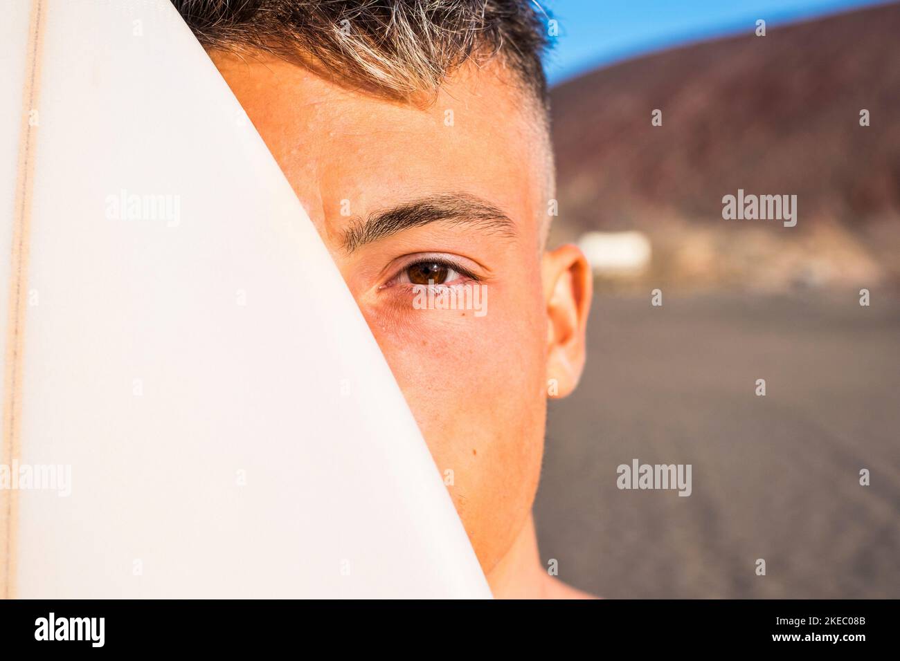 close up and portrait of one young and handsome man with a surfboard covering an half of his face - active teenager lifestyle Stock Photo