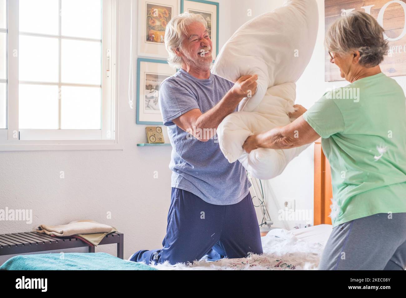 couple of two happy seniors having fun playing together on the bed at home fighting with pillows enjoying - pillows war indoors in the morning Stock Photo