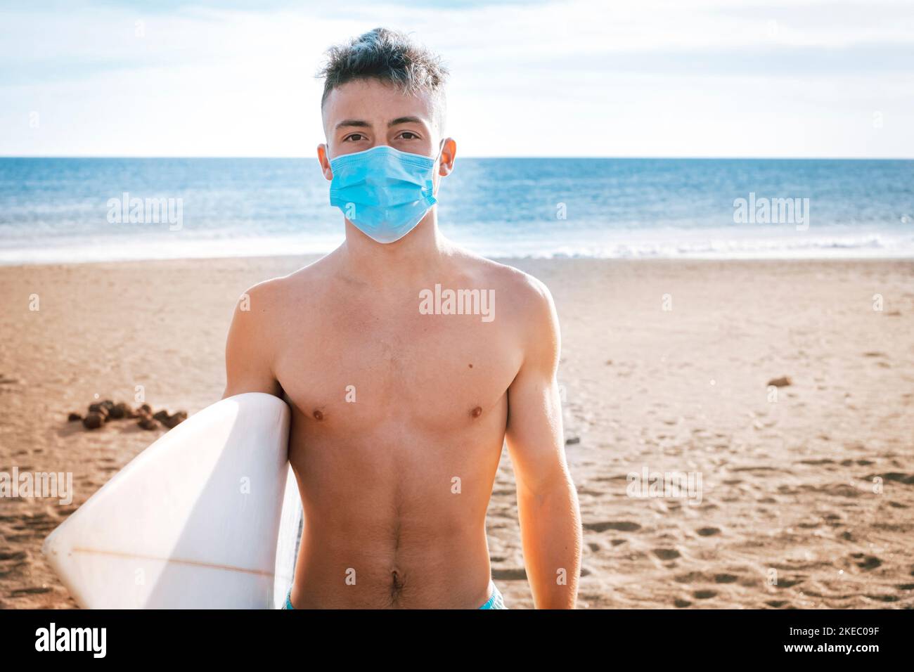 close up and portrait of young man or teenager looking at the camera seriously wearing mask to prevent disease and virus surfing for the contamination of the sea and the ecology of the nature Stock Photo