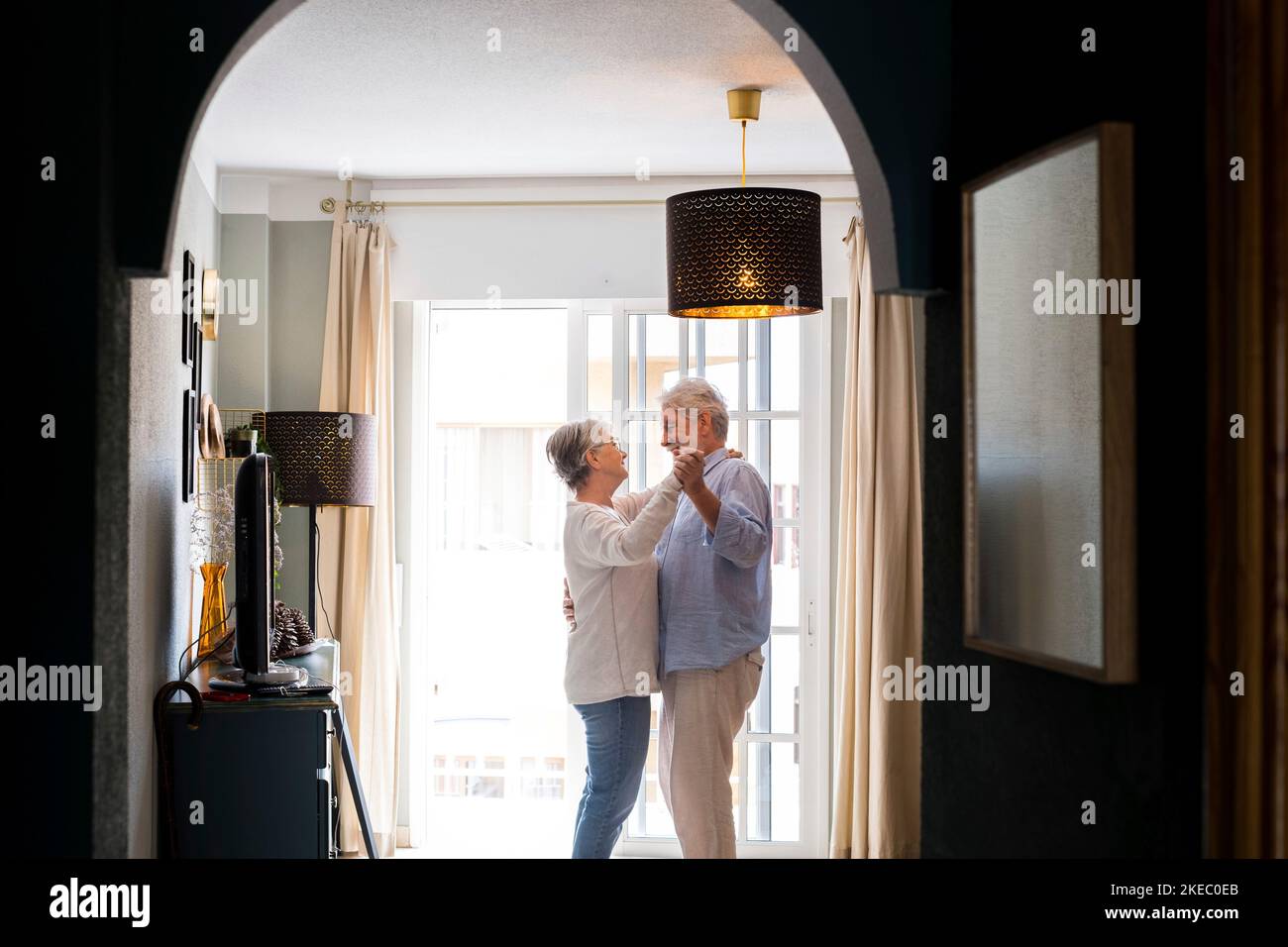 Romantic loving senior couple holding hands enjoying dancing together in the living room of house, couple embracing while holding hands together at home Stock Photo