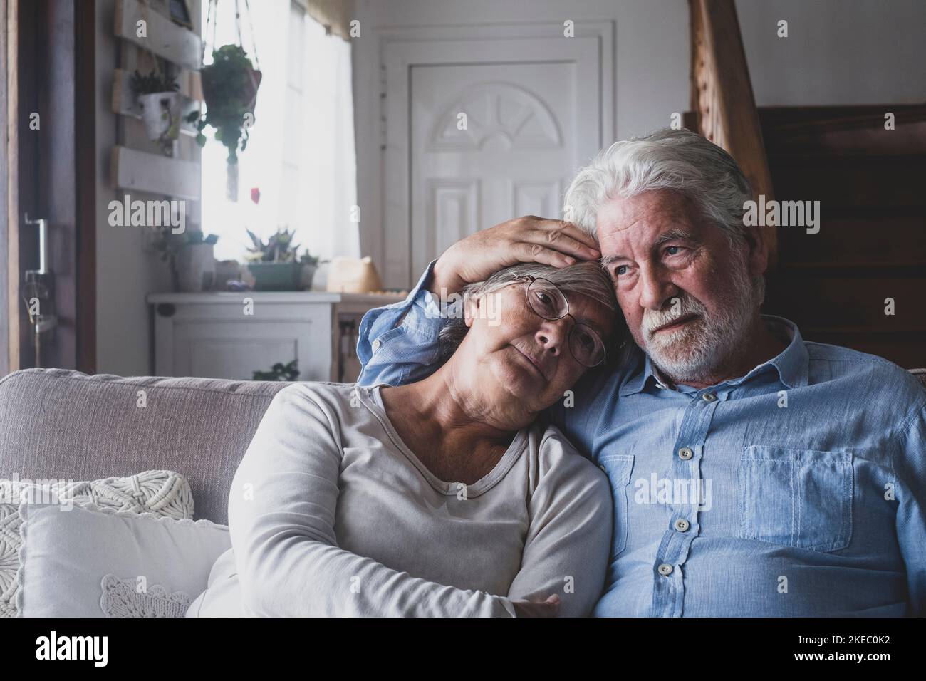 Thoughtful sad senior man and woman relaxing on sofa in the living room of modern house. Retired couple comforting each other from depressed emotion while sitting on couch at home Stock Photo