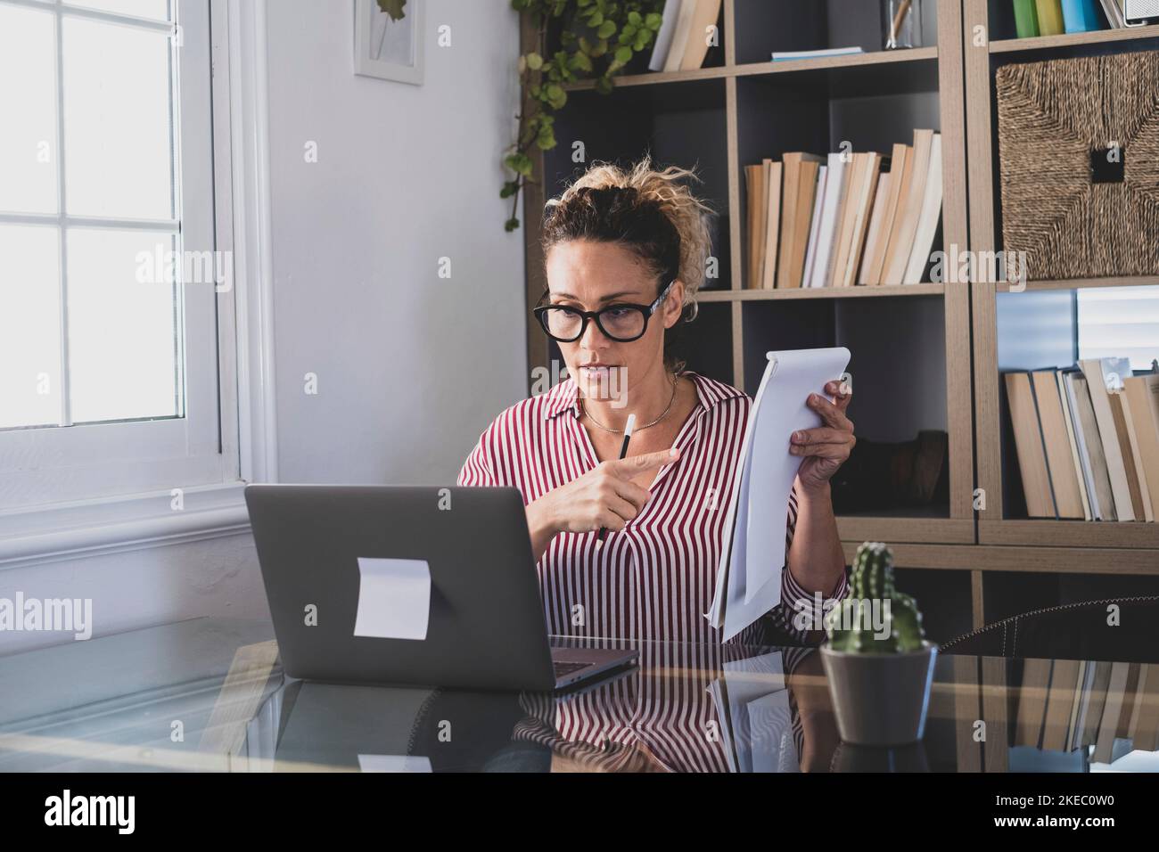 Happy young caucasian businesswoman smiling working online watching webinar podcast on laptop and learning education course conference calling make notes sit at work desk, elearning concept Stock Photo