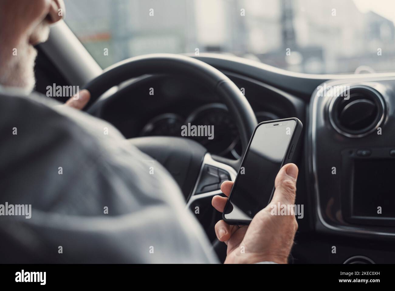 Man looking at mobile phone while driving a car. Old pensioner person distracting texting and chatting. Stock Photo