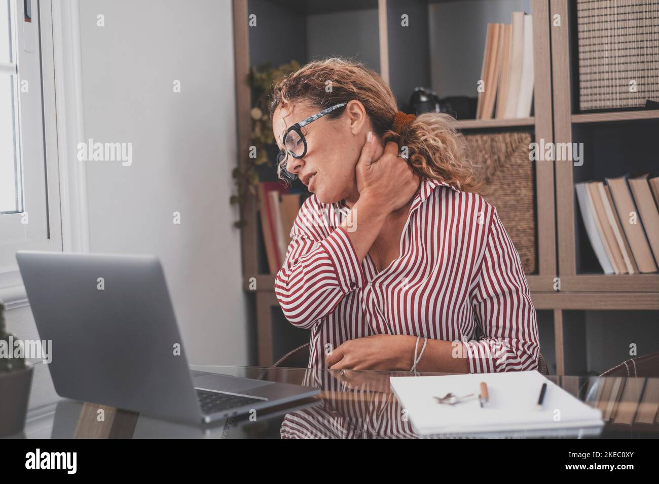 Pinched nerves, tensed sore muscles, fibromyalgia ache due sedentary lifestyle and incorrect posture concept. Caucasian ethnicity frowning woman sitting at desk in front of laptop, touch neck feels pain Stock Photo