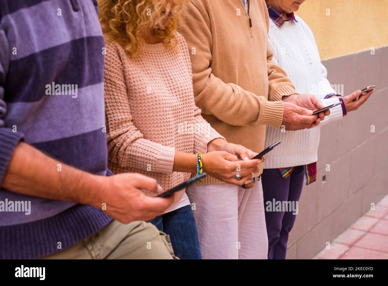 close up and portrait of four people using their phones together in the street chatting or texting and surfing on the net - social media and network concept annd addicted lifestyle Stock Photo