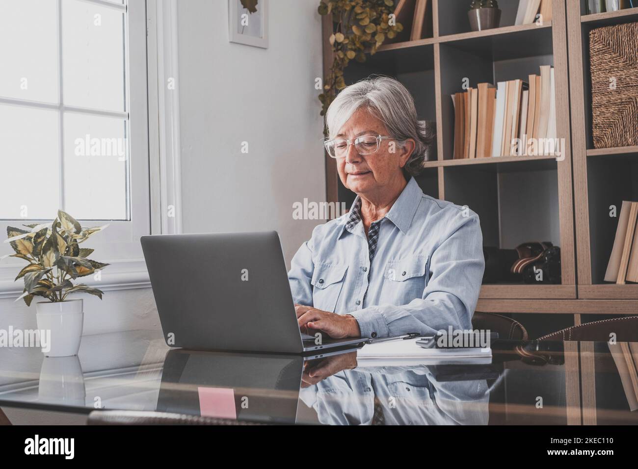 Happy old caucasian businesswoman smiling working online watching webinar podcast on laptop and learning education course conference calling make notes sit at work desk, elearning concept Stock Photo