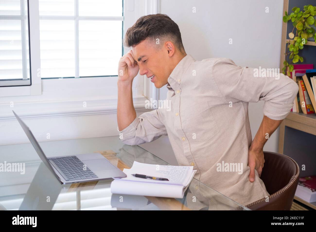 Close up rear view stressed young man touching lower back feeling discomfort, suffering from sudden pain due to sedentary lifestyle or long computer overwork in incorrect posture at home office. Stock Photo