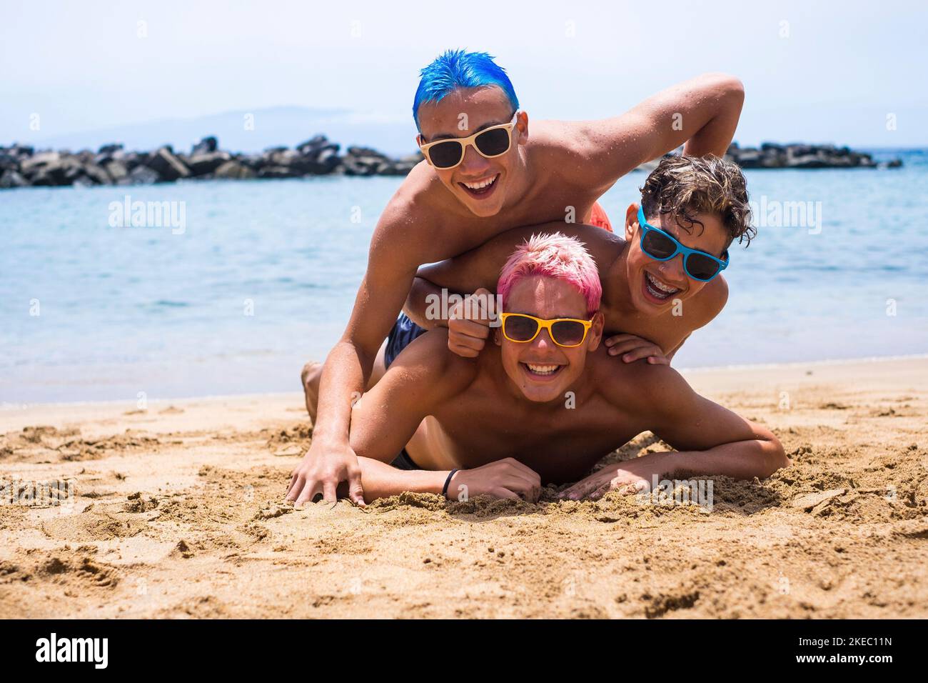 group of three friends having fun playing and enjoying together at the beach wearinng sunglasses laughing smiling and looking at the camera - teenager with different colors of hair enjoying summer and vacations Stock Photo
