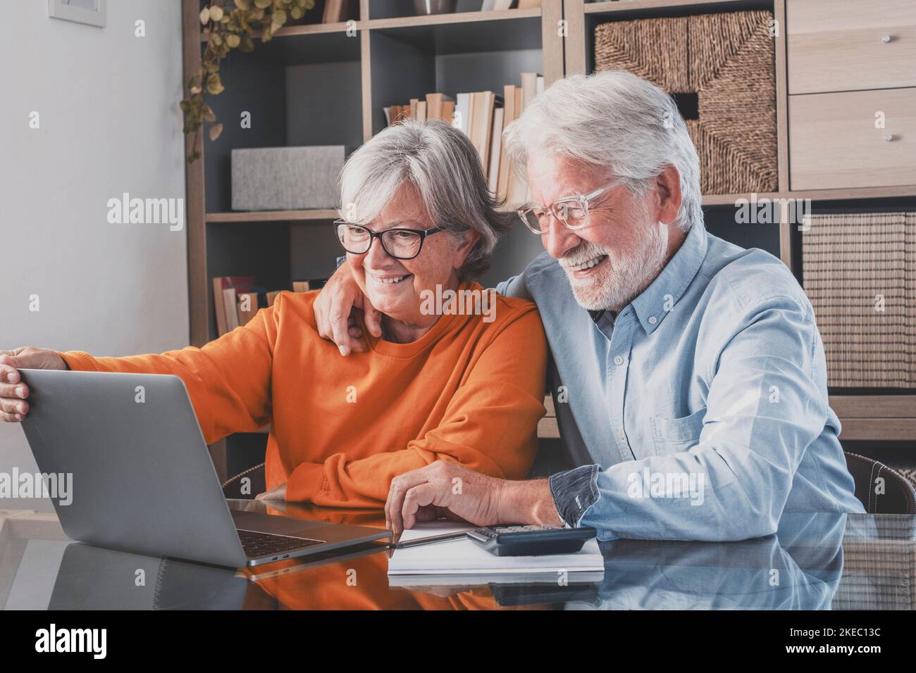 Elderly man and woman having fun using laptop at office. Smiling old husband and wife doing home finance online. Senior couple watching media content and enjoying at home Stock Photo