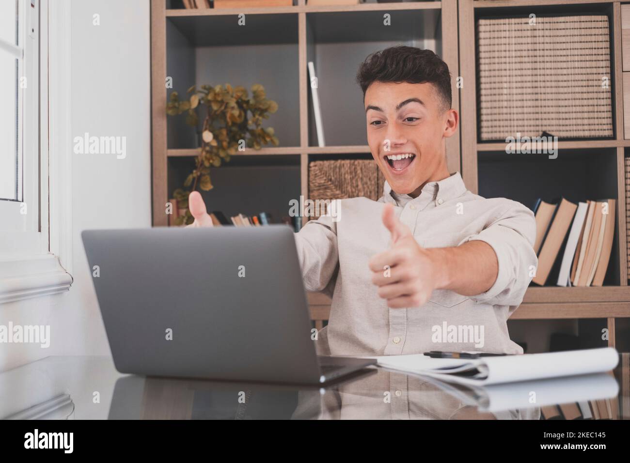 Overjoyed caucasian ethnicity teenager sit at desk looks at laptop screen read incredible news clench fists makes yes gesture celebrate on-line lottery gambling win, getting new job offer feels happy Stock Photo